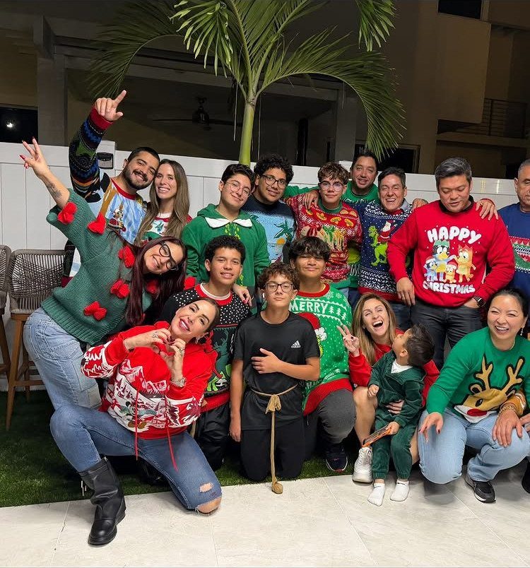Group of people wearing colorful ugly Christmas sweaters posing together outdoors at night.