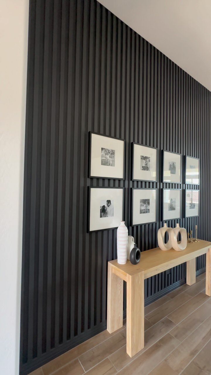 Black slatted accent wall with framed photos and a light wood console table.