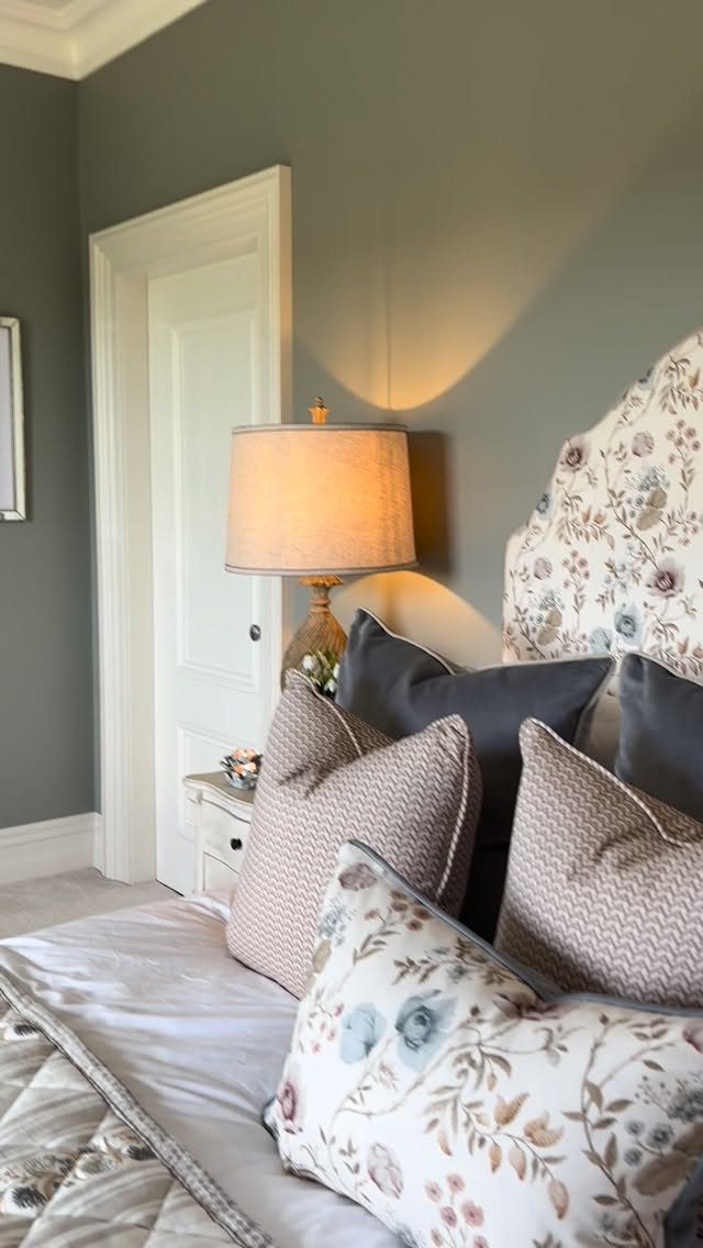Decorative cushions and a floral pillow on a bed next to a glowing lamp.