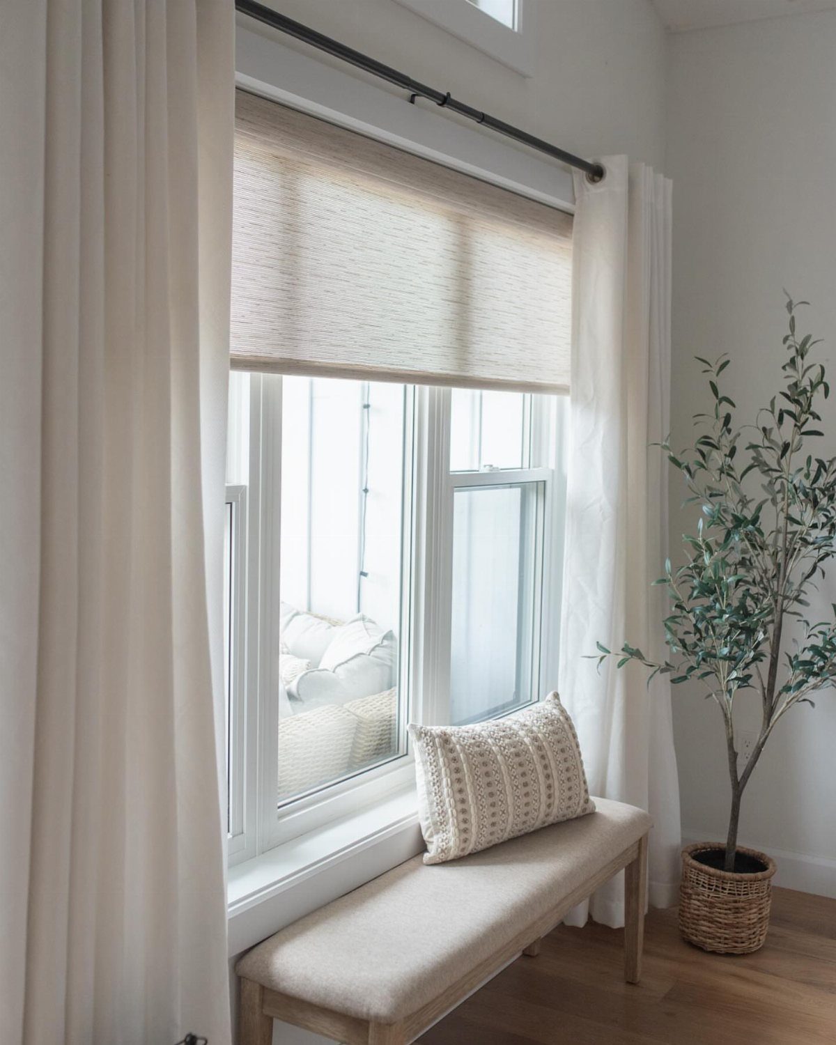 White sheer curtains and a beige roman shade on a bright window