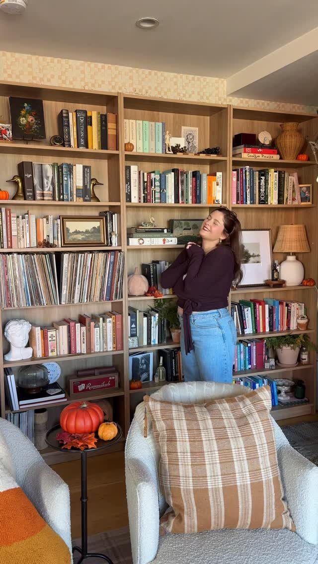 Tall light-wood bookcases filled with books and decor behind a smiling woman.