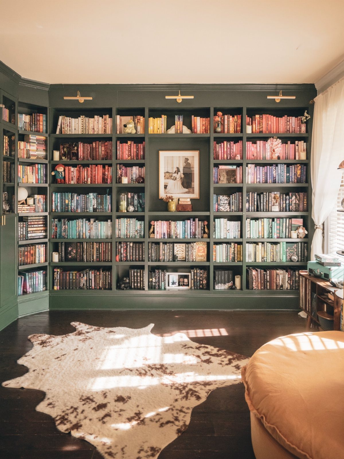Dark green built-in bookshelves filled with color-coded books and a cowhide rug.
