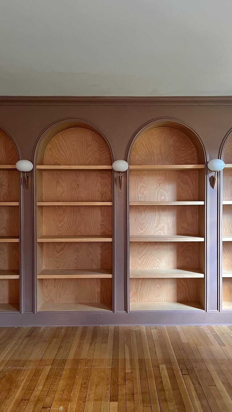 Arched built-in wooden bookshelves with mauve trim and small globe lighting above hardwood floors.