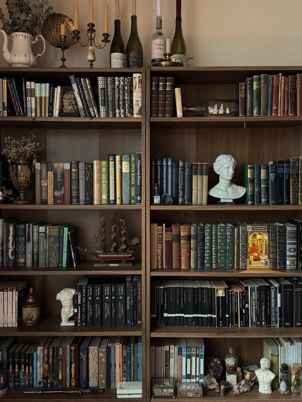 Dark wood bookshelves filled with old books and decorative busts, ships, and bottles.