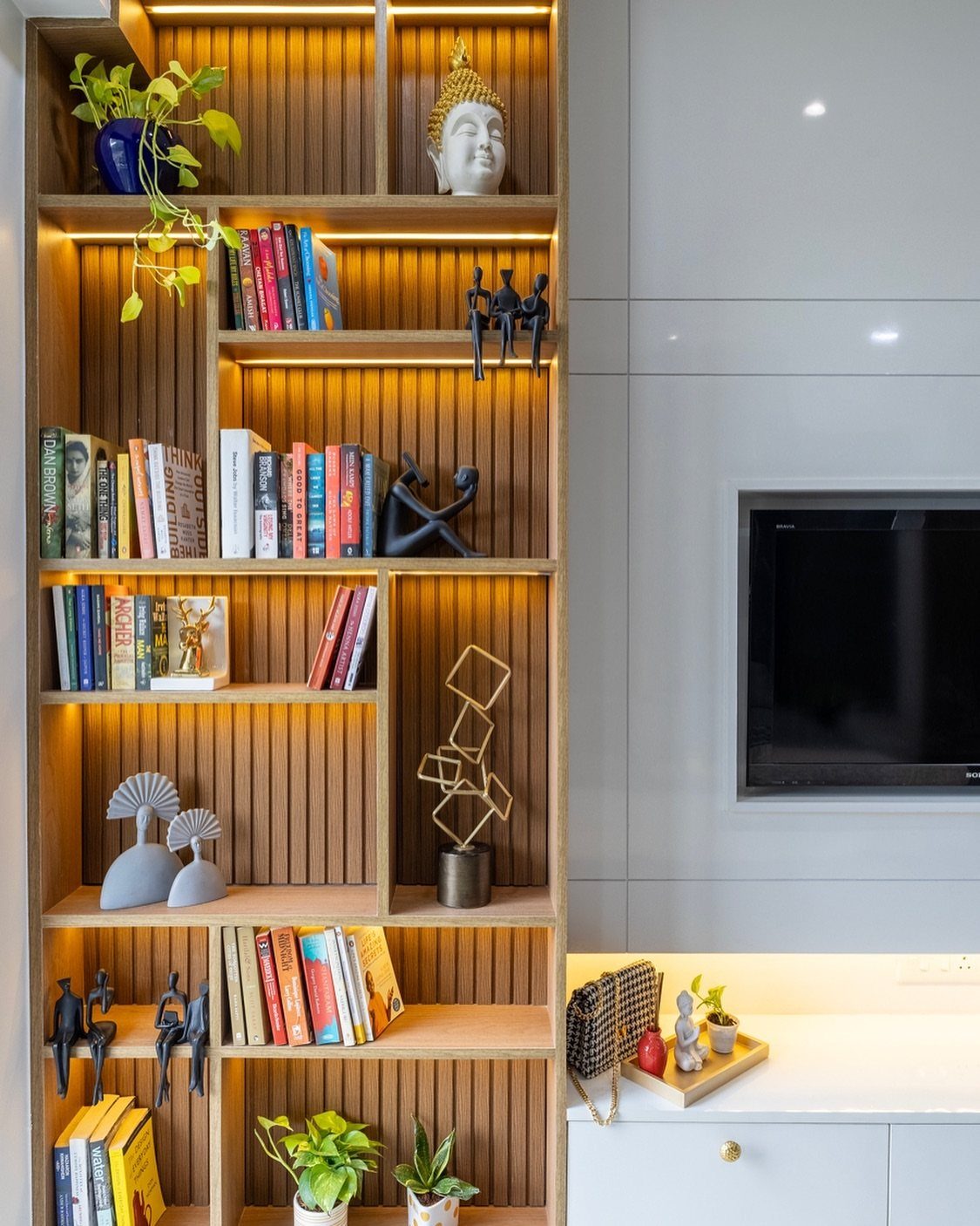 Light wood modular shelving unit with integrated lighting, books, and decorative art objects.
