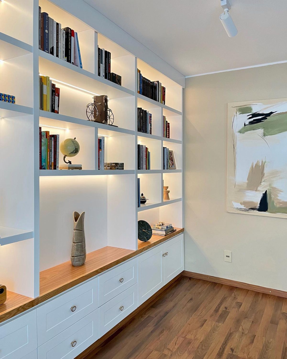 White built-in bookcases with integrated lighting and a light wood countertop on hardwood floors.