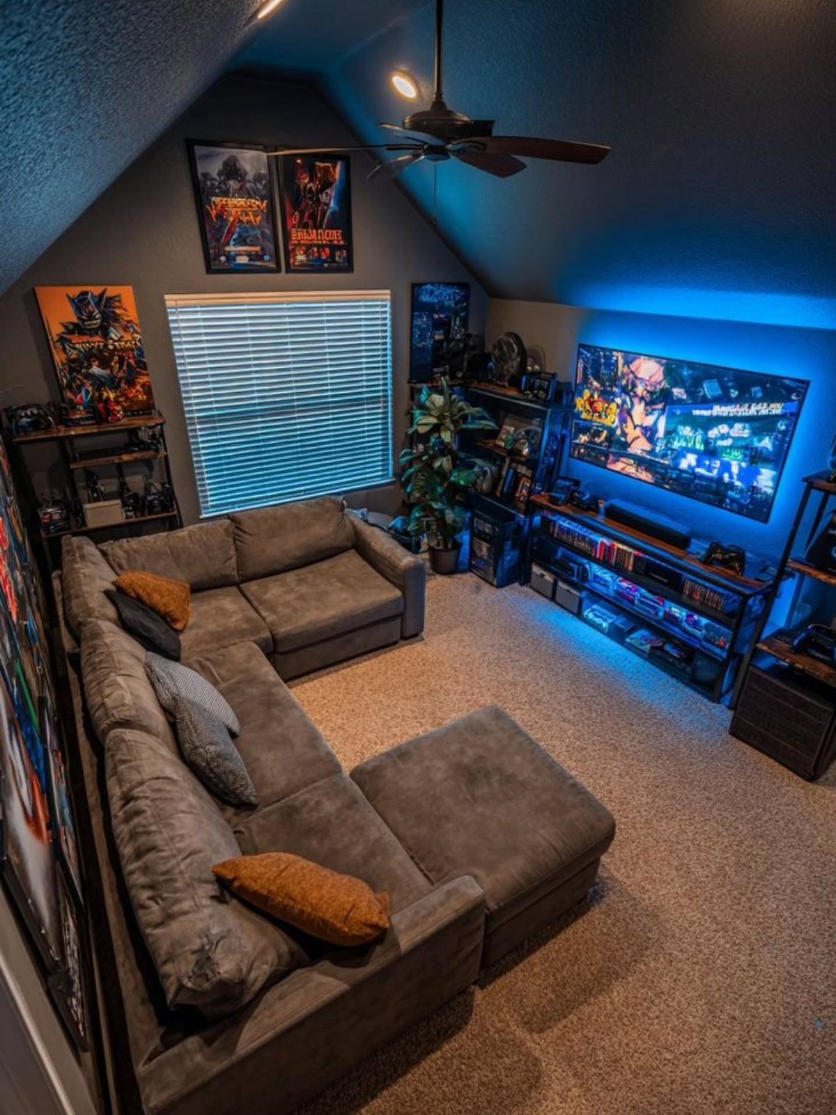 Grey sectional sofa facing a large screen with blue lighting and gaming memorabilia.