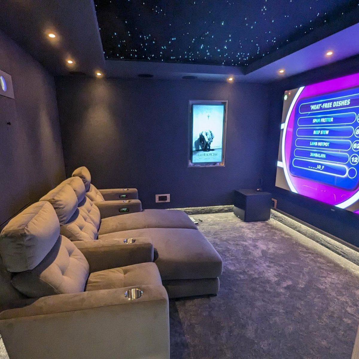 Grey reclining theater seats in a room with a starry ceiling and screen.
