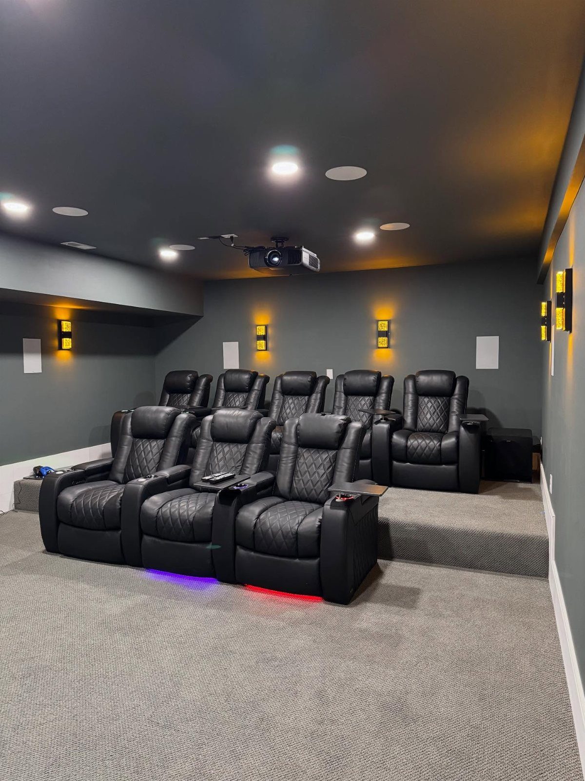 Black leather reclining theater seats in a dark grey room with accent lighting.