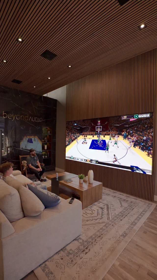 Modern home theater with wooden slat walls, large screen, and light-colored sofa.