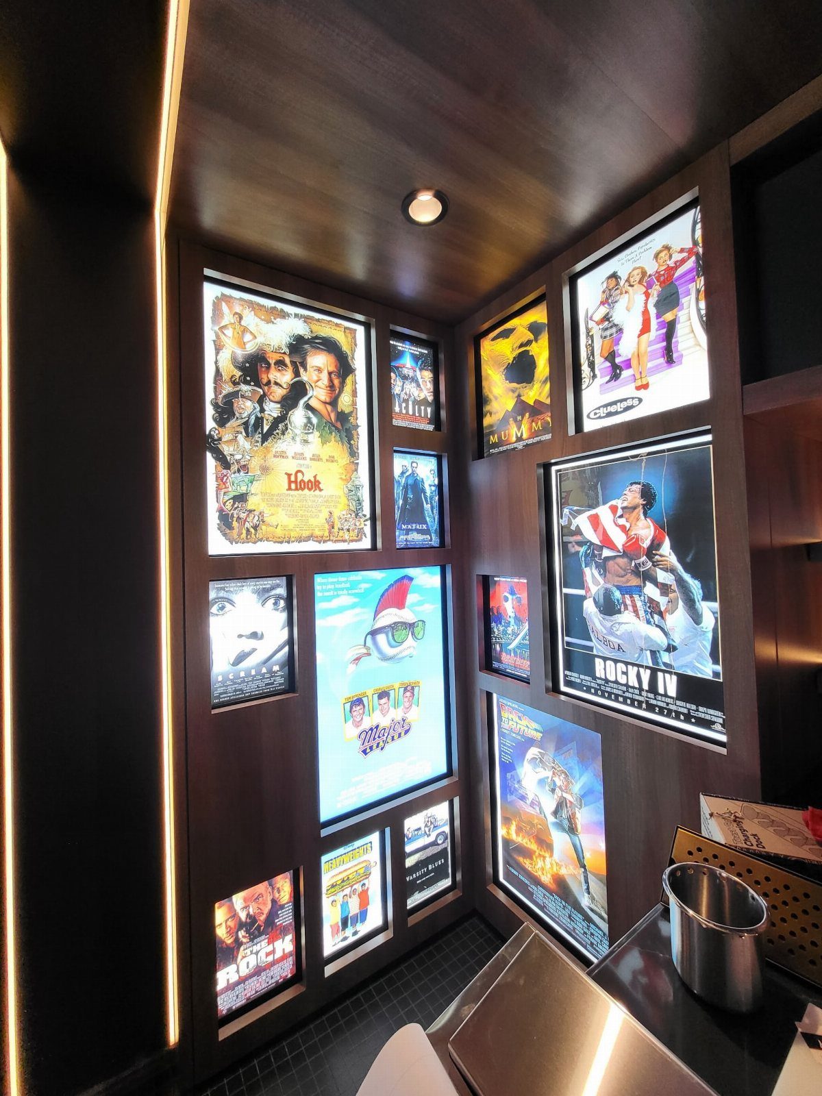 Backlit movie posters displayed on dark wood walls in a home cinema room.