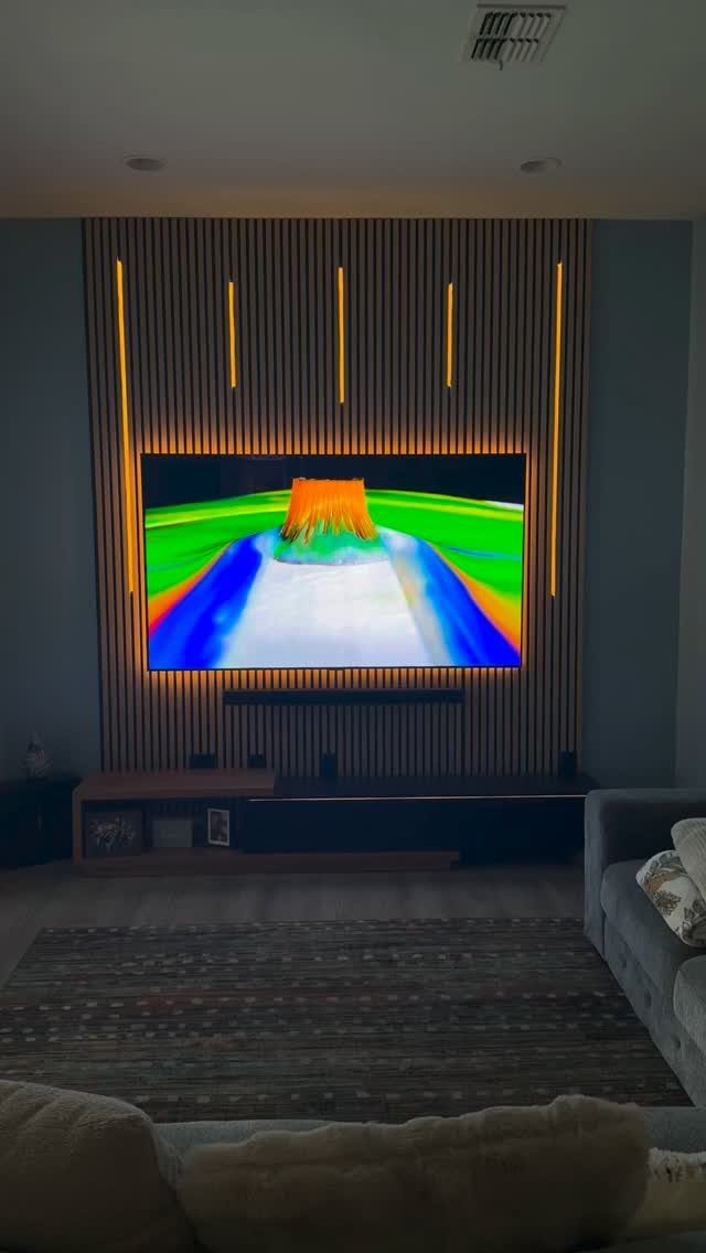Television mounted on a wooden slat wall with integrated vertical yellow LED strip lighting.