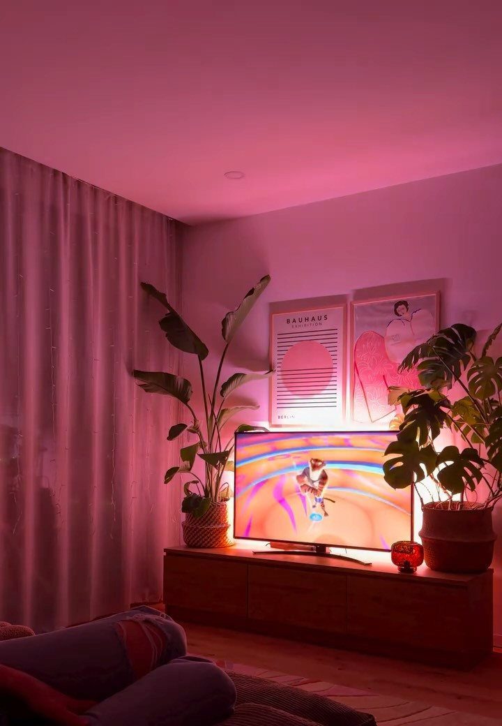Living room with pink ambient lighting, a television, and backlit wall art.