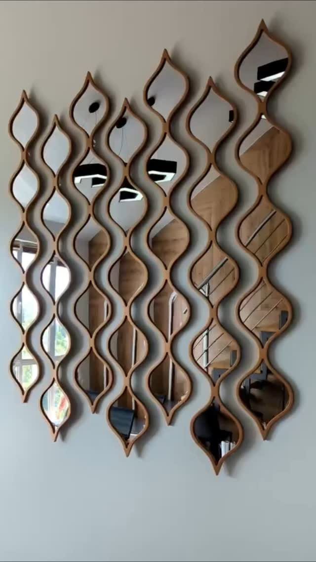 Wavy teardrop-shaped mirrors with wooden frames arranged in columns on a white wall.