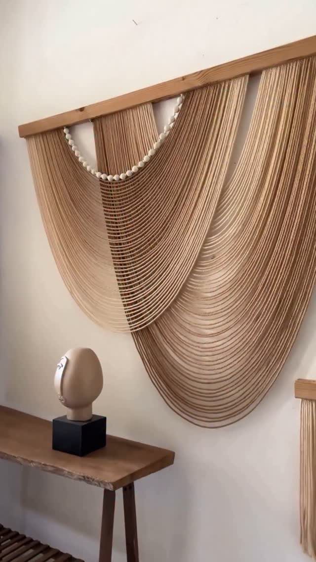 String art wall hanging with draped brown cords and white beads on white wall