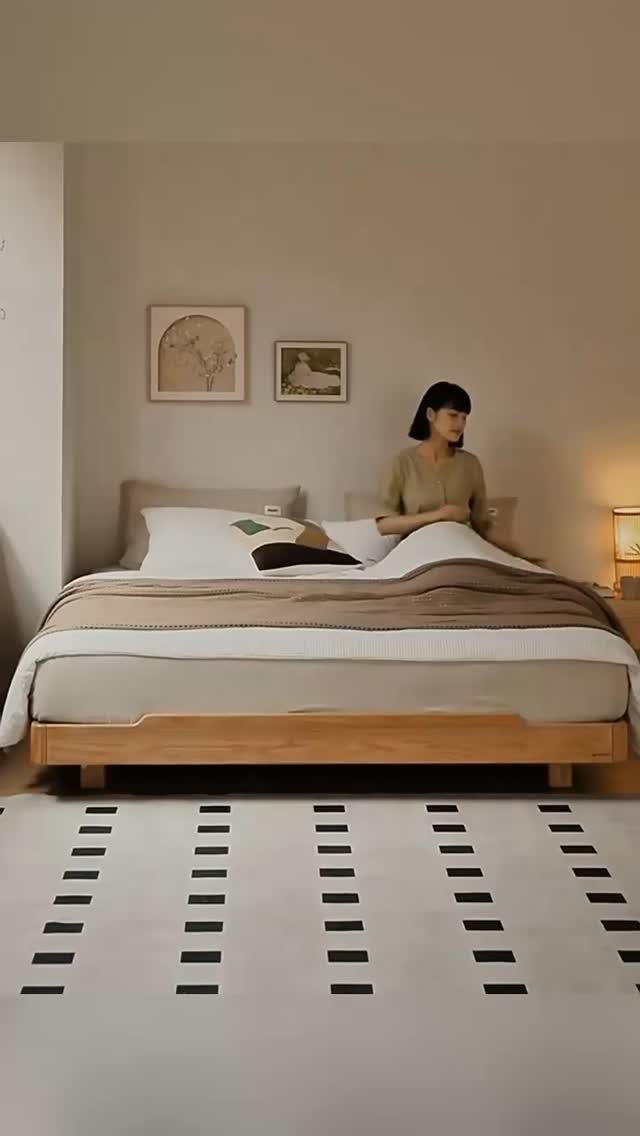 Woman sitting in a minimalist bedroom with neutral tones and wooden furniture.