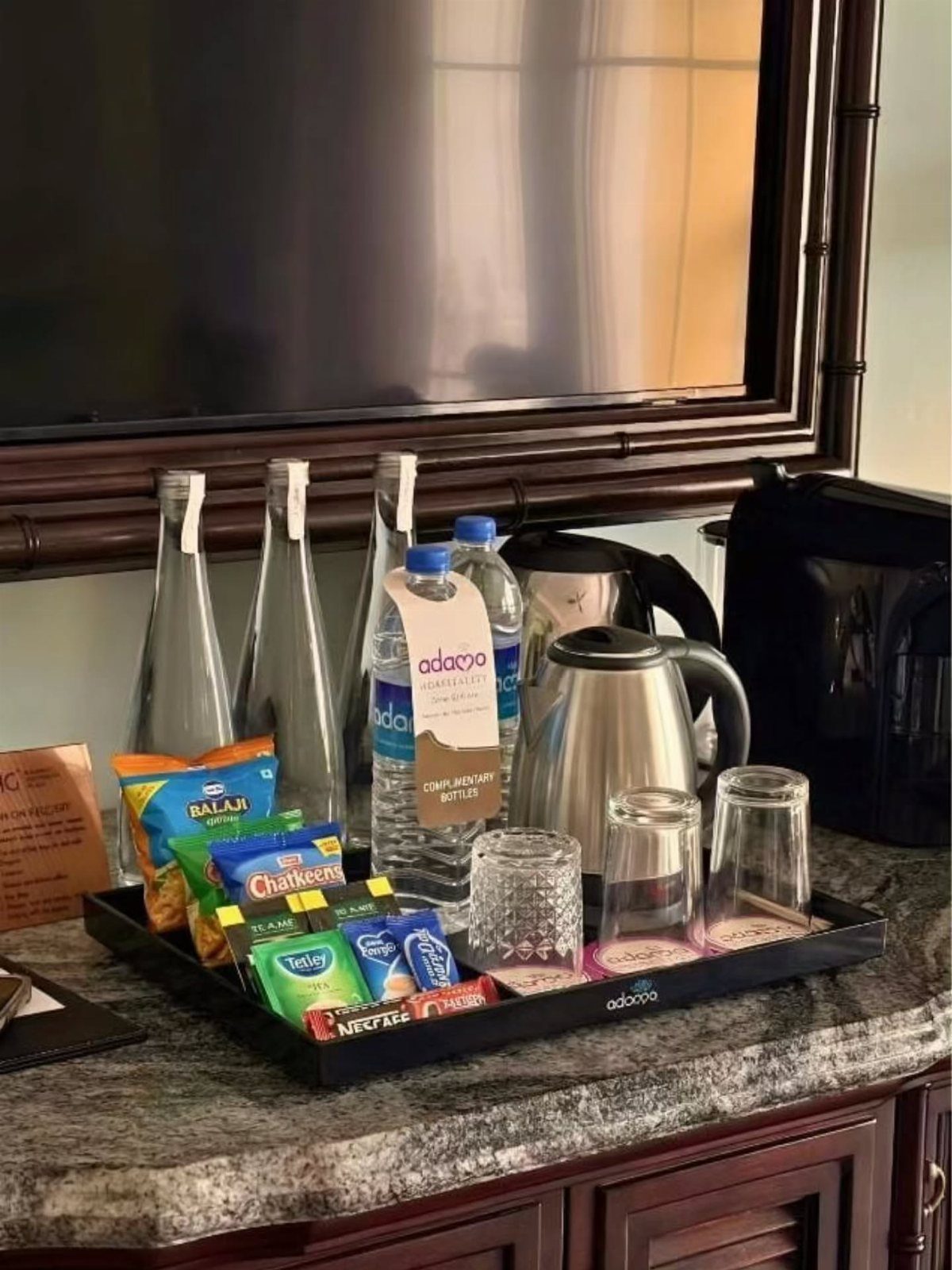 Black tray with bottled water, snacks, and a kettle on a granite counter.