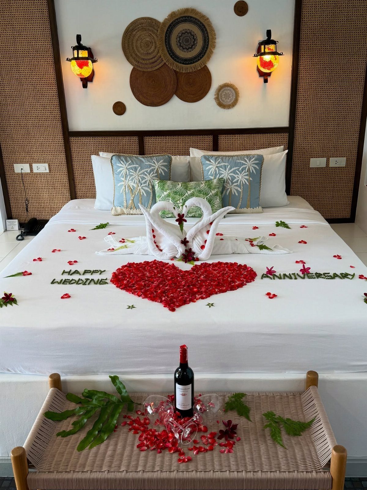 Hotel bed decorated with towel swans and red flower petals for a wedding anniversary.