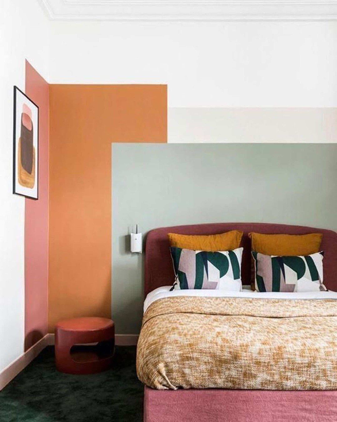 Bedroom wall painted with overlapping geometric blocks of orange, terracotta, and sage green.