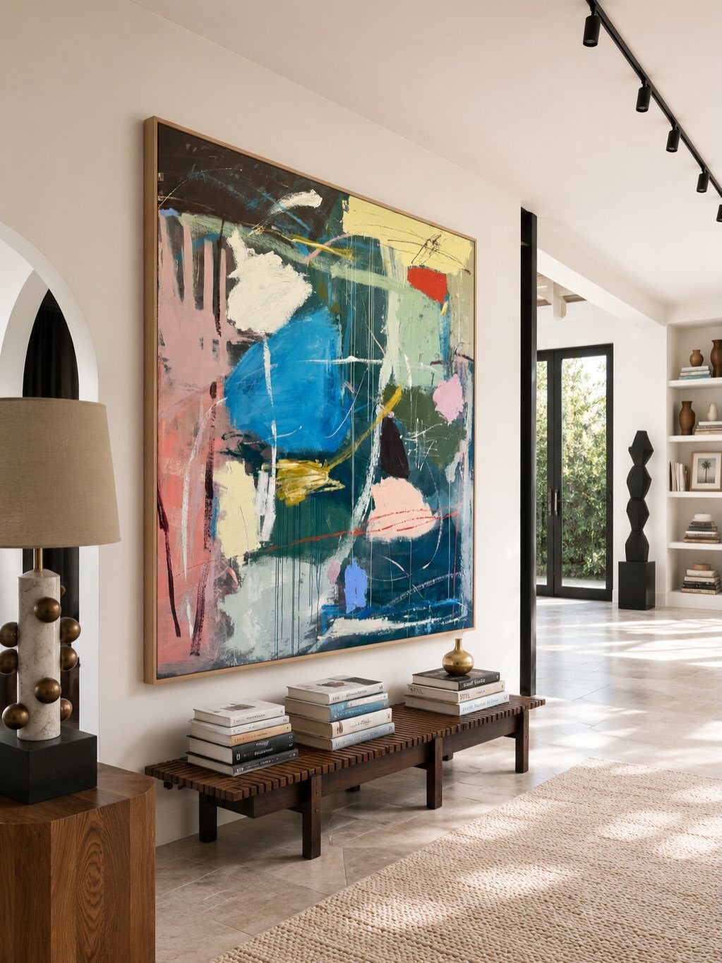 Large abstract painting with blue and pink tones hanging above a wooden bench.