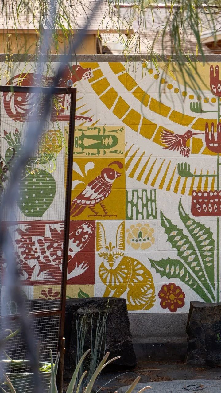 Colorful mural with stylized birds and plants painted on a white exterior wall.