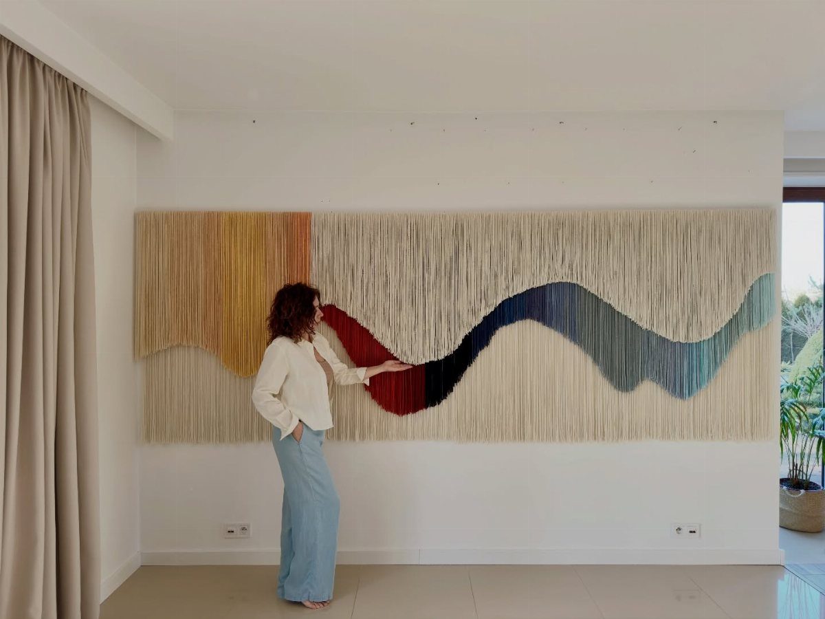 Large colorful textile wall hanging with a woman standing beside it in a room.
