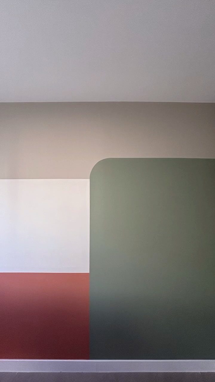 Wall painted with geometric color blocks in beige, white, red, and sage green.