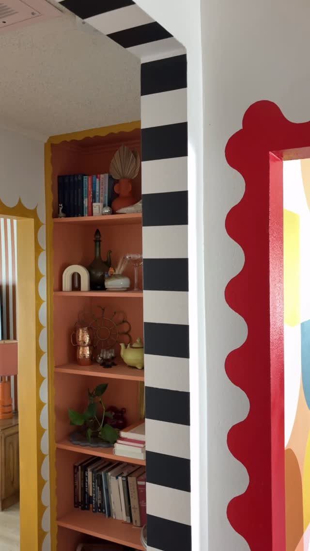 Colorful painted wall borders and striped doorway framing a room with orange bookshelves.