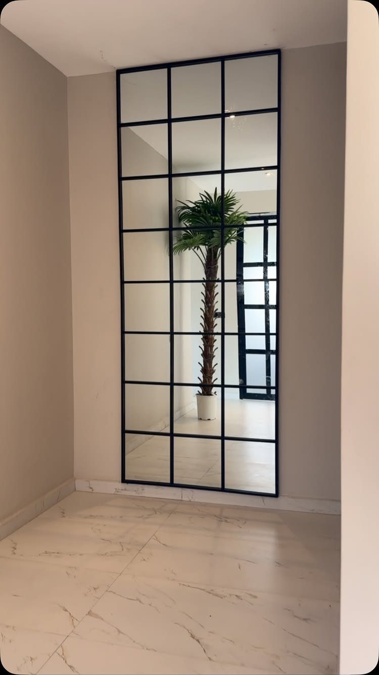 Large rectangular mirror with black grid frame reflecting a room with a palm tree.