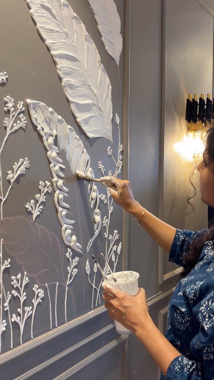 Woman applying white 3D textured floral relief art to a large grey wall