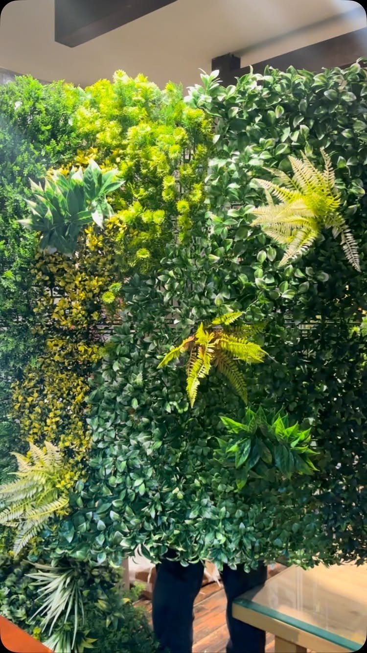 Vertical garden wall with lush green artificial leaves and ferns in an indoor setting.