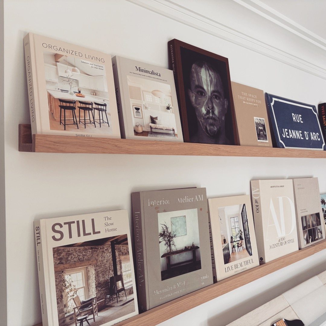 Wooden floating shelves on a white wall holding books and a framed portrait.