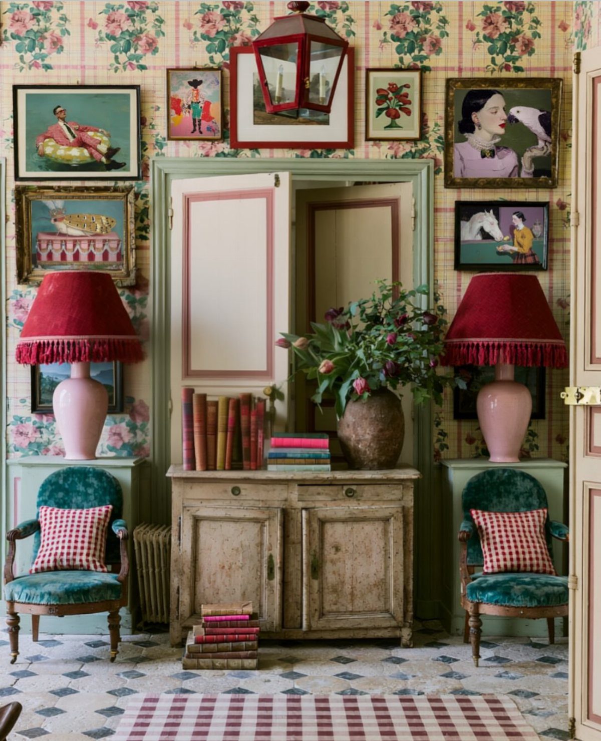 Vintage framed paintings and a red lantern on floral wallpaper above a rustic cabinet.