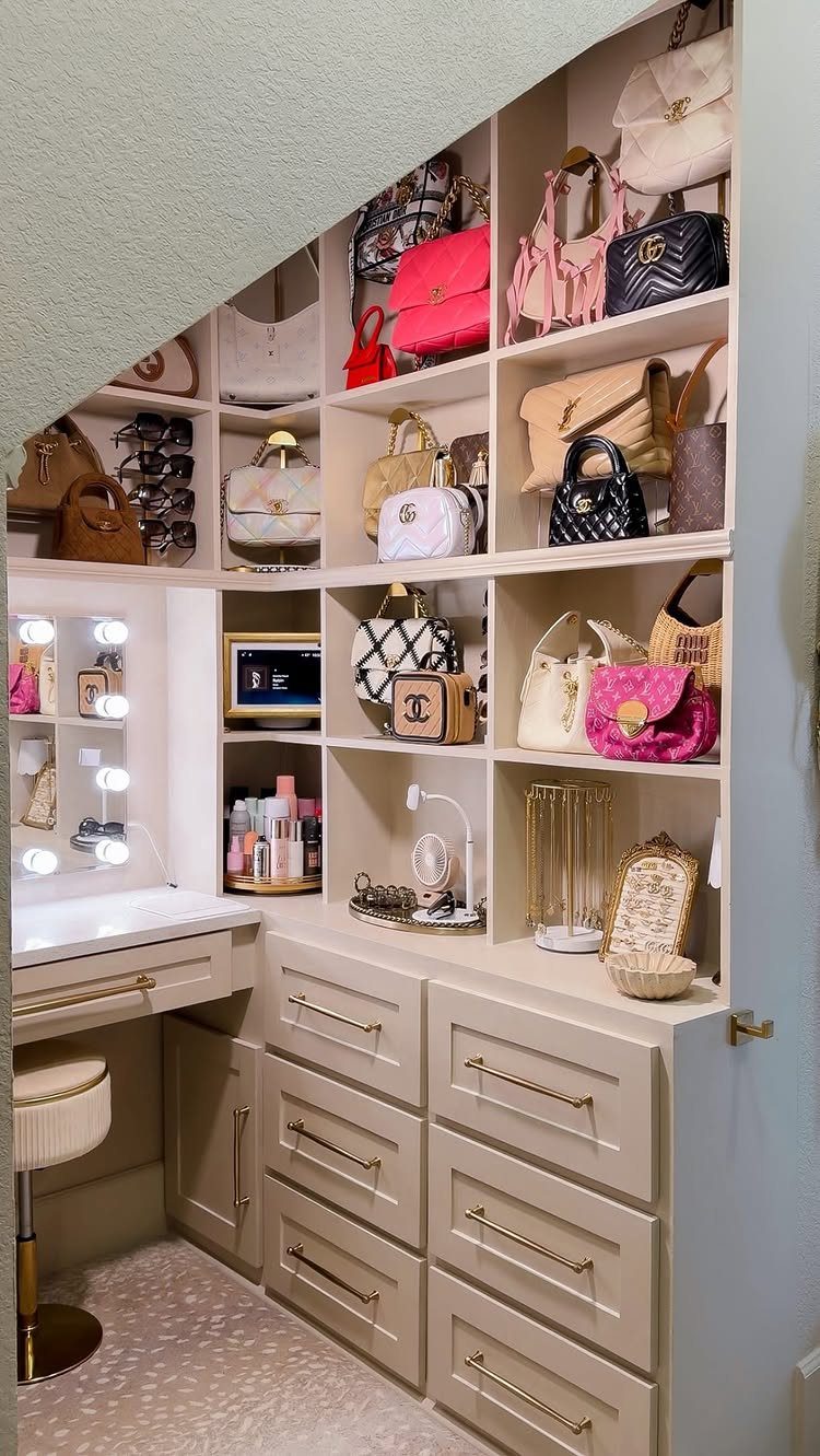 Built-in beige closet with open shelving for handbags and a lighted vanity desk.