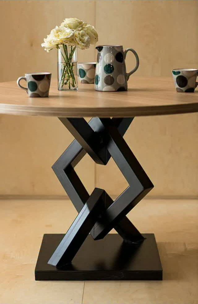 Round wooden table with a black geometric base and polka dot ceramics.