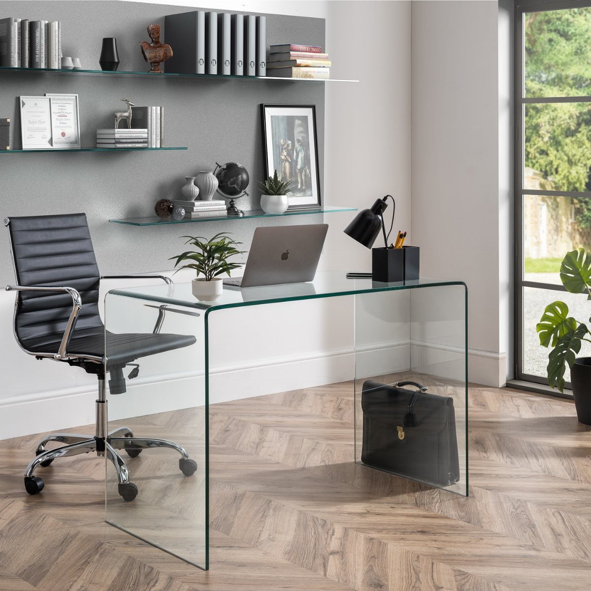 Clear glass desk with a black leather chair in a modern office setting