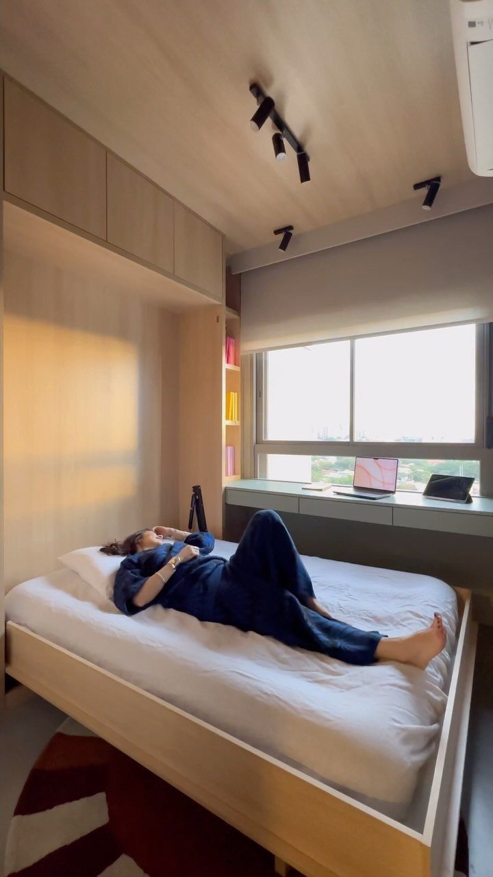 Person resting on a bed in a multifunctional guest room and home office space.