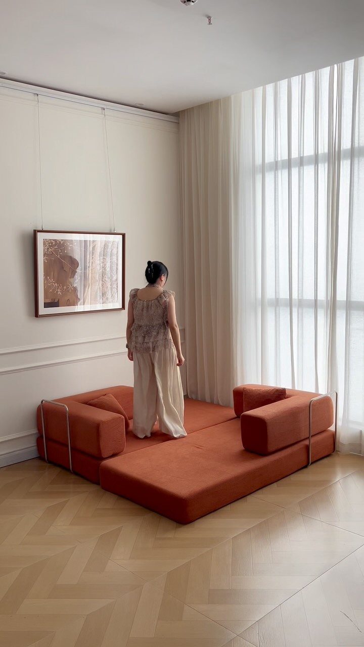 Modern apartment interior with an orange modular sofa and herringbone wood flooring.