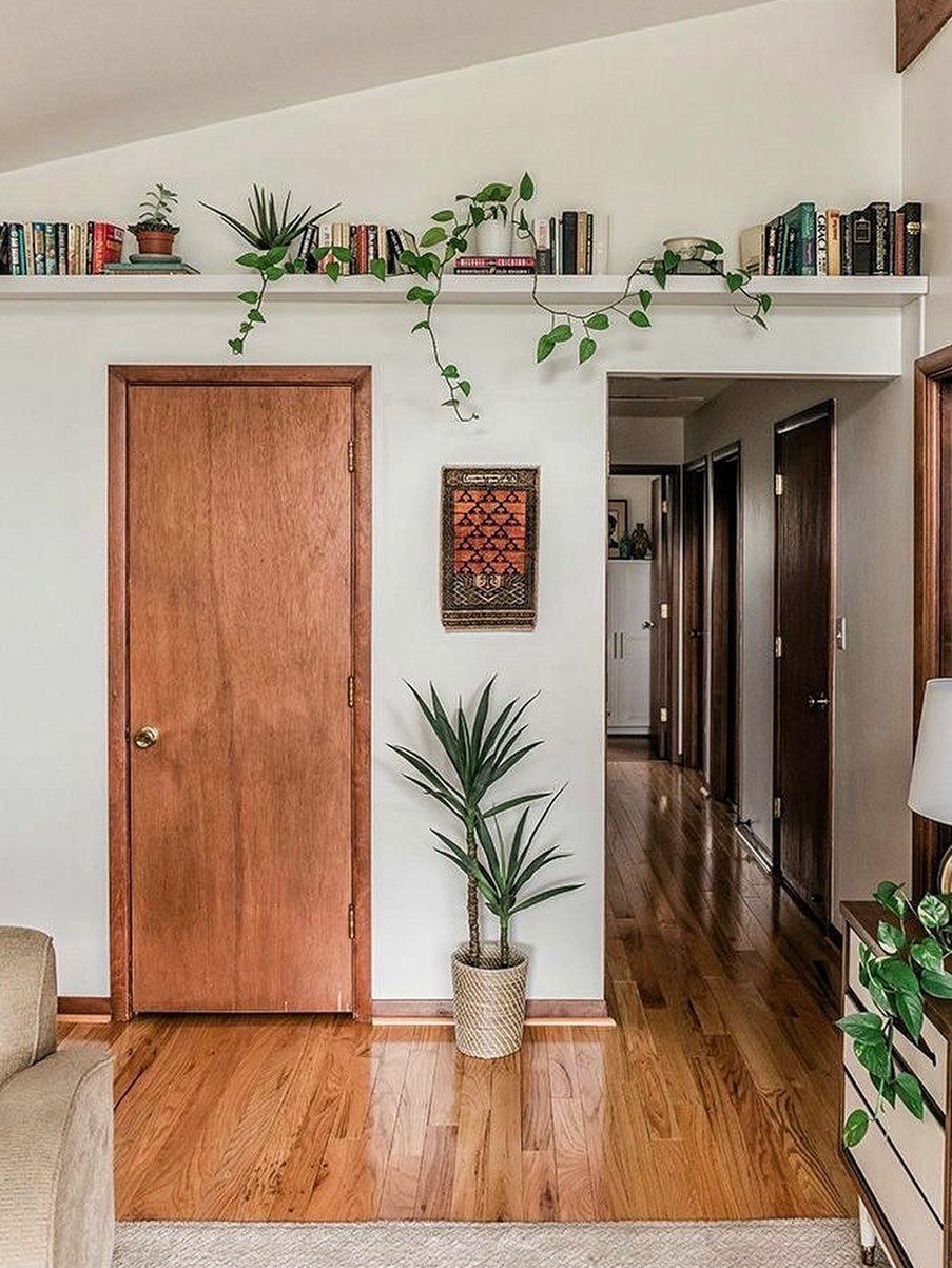 High white wall shelf with books and plants above wooden doors and hardwood floors