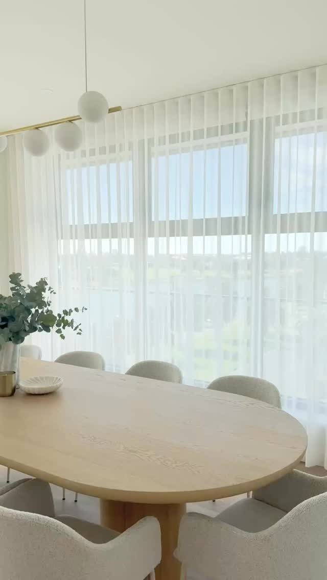 Light wood dining table with cream chairs in a bright, neutral white room.