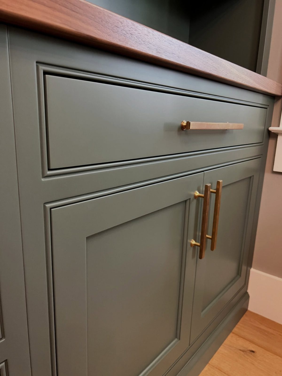 Sage green kitchen cabinets with gold handles and a wooden countertop.