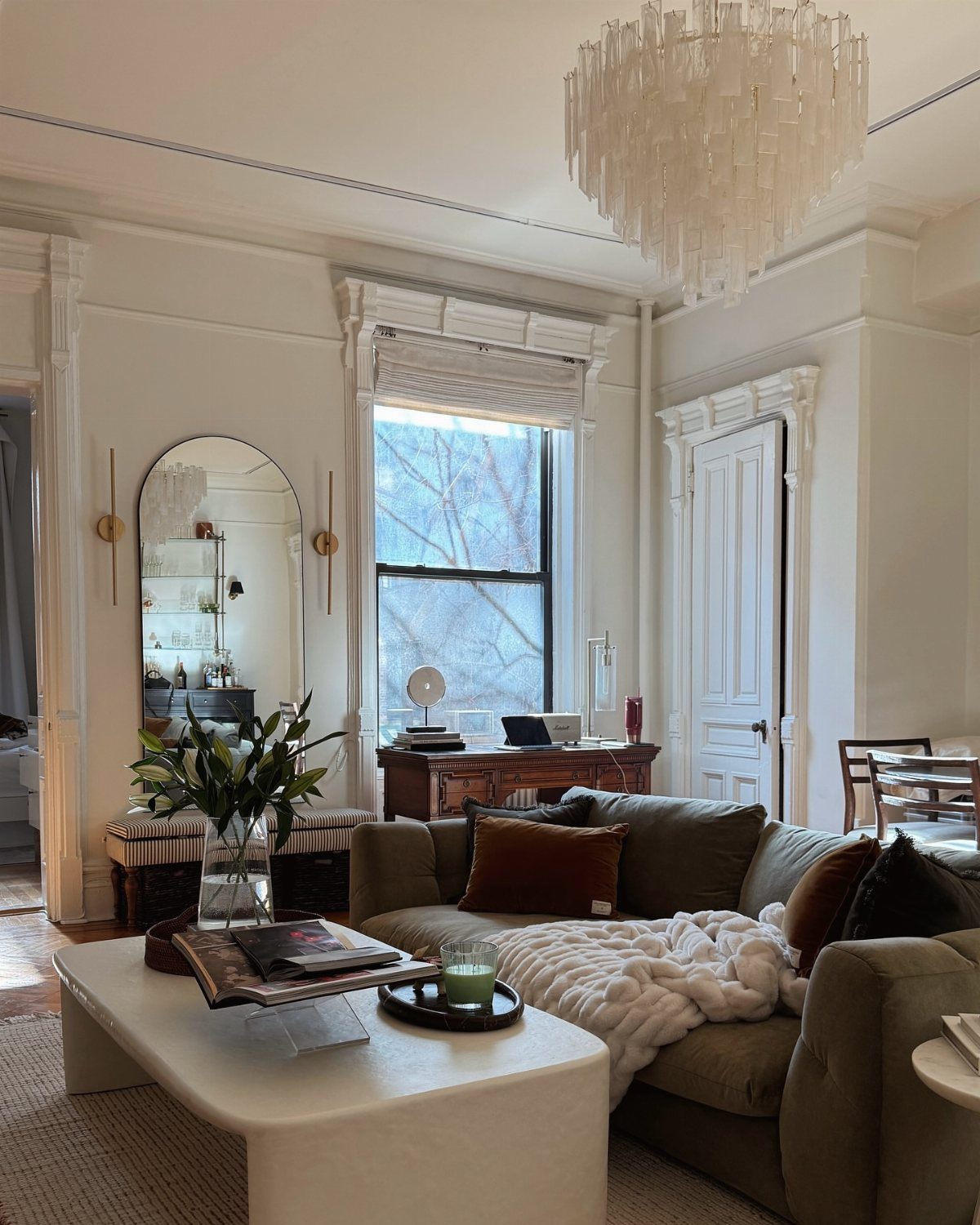 Bright living room with green sofa, white coffee table, and crystal chandelier.
