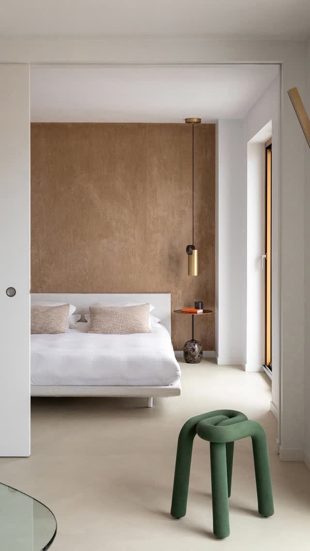 Modern bedroom with a brown textured accent wall and a green sculptural stool.