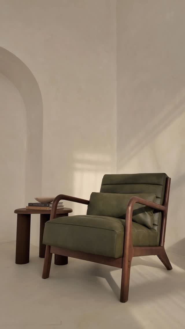 Olive green armchair with wooden frame and pillow in a minimalist room
