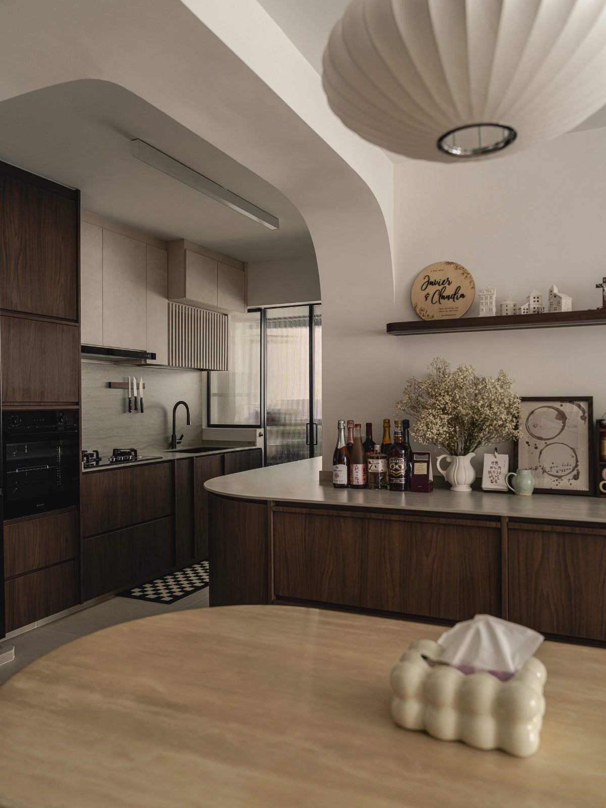 Modern kitchen with dark wood cabinets, white walls, and a large pleated lamp.