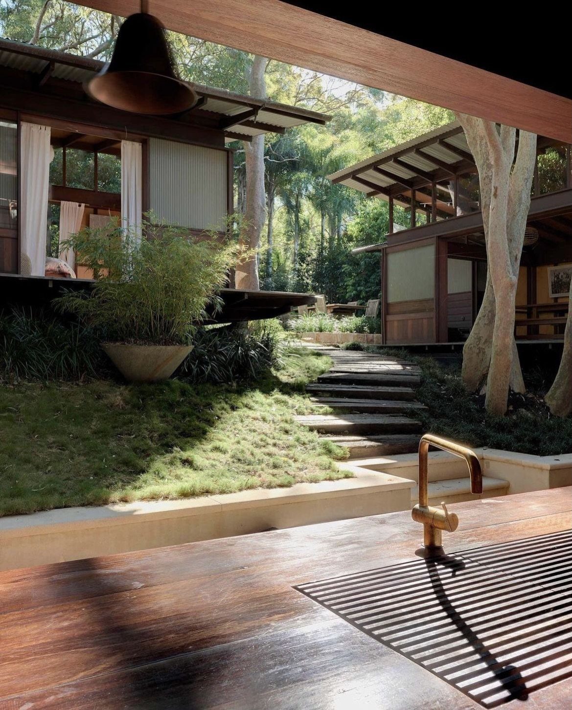 Wooden outdoor kitchen counter overlooking a lush green garden with stone steps and trees.