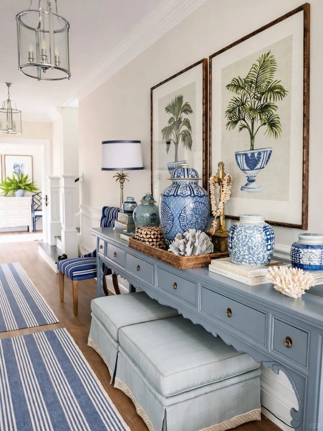Light blue console table with blue ceramics and framed green palm leaf prints.