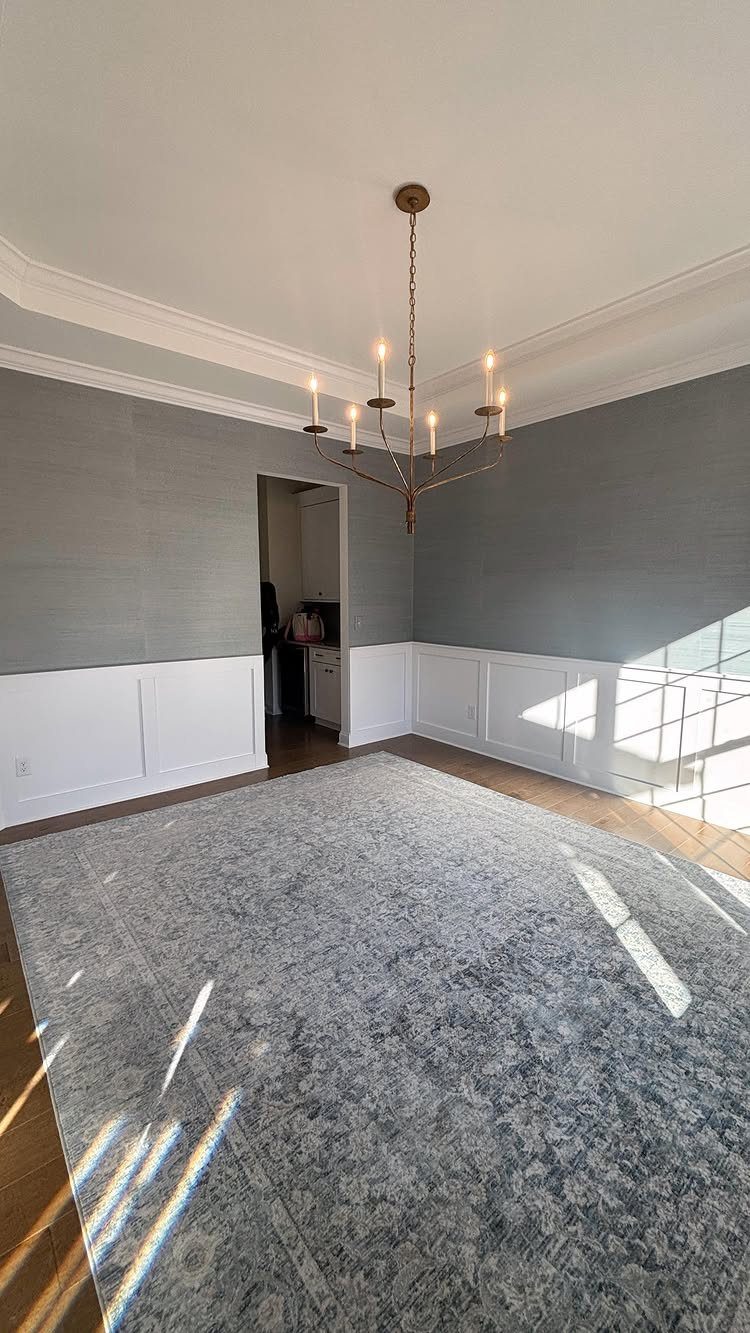 Light blue walls and white wainscoting with a large blue area rug and chandelier.