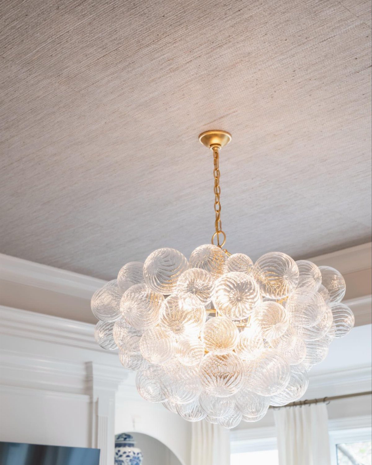 Gold chandelier with glass globes hanging from a textured grey grasscloth ceiling