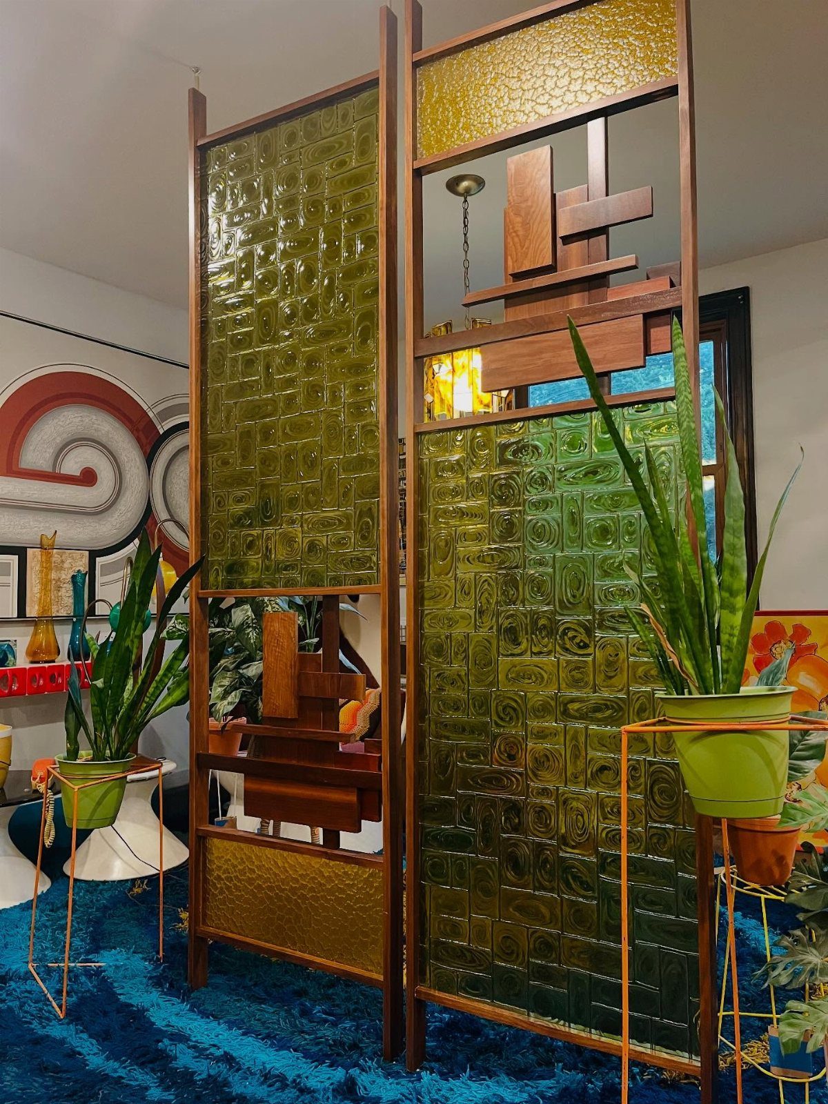 Wooden room divider with green glass panels over a blue shag rug.